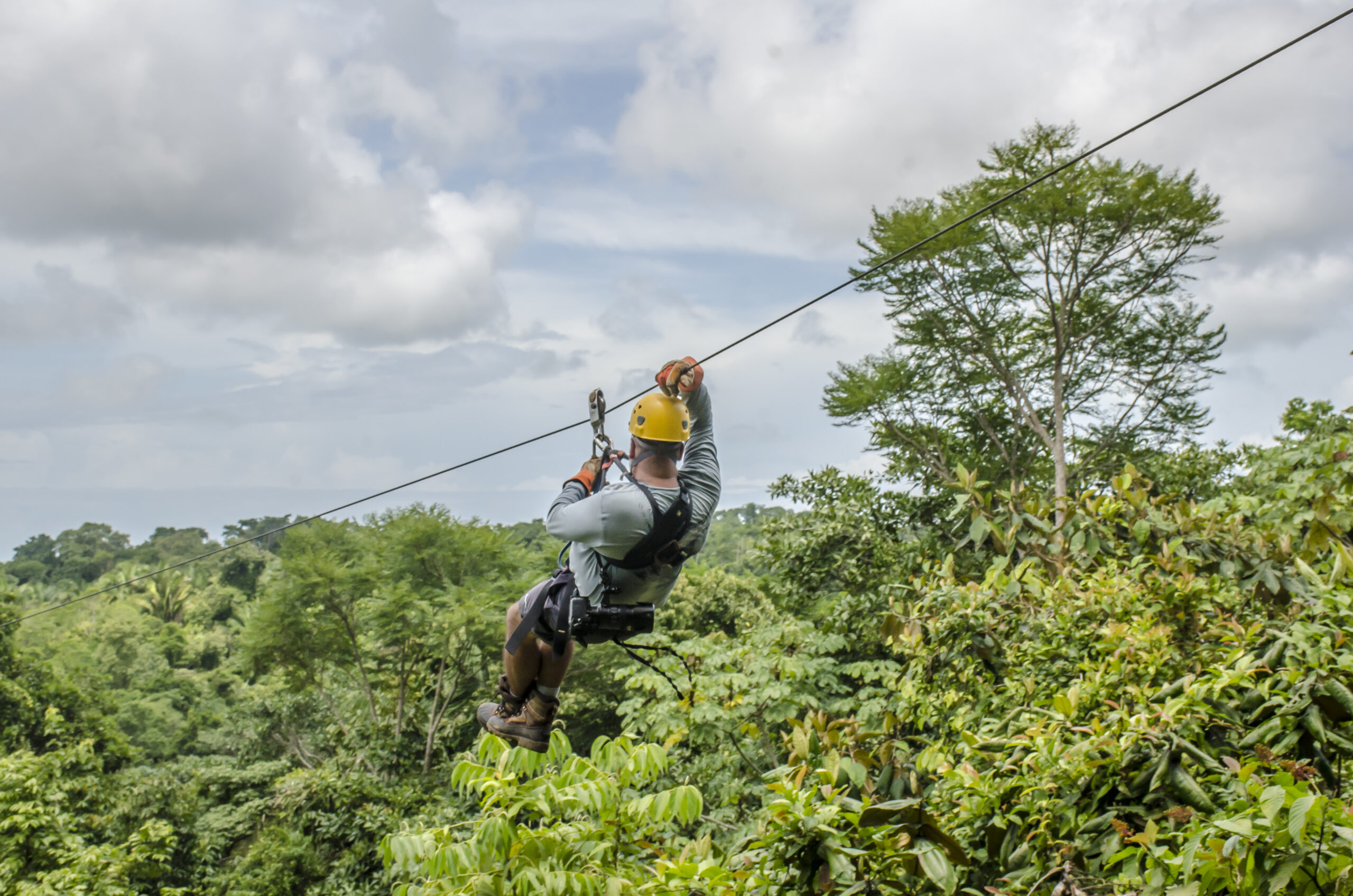 A close up shot of a man hanging and sliding on the zipline in a beautiful park, cloudy sky